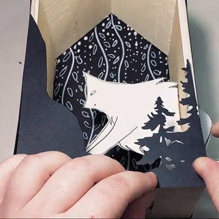 Home is Where the Niche is Wood shadow box in the shape of a house with silhouette cutouts of trees and a wolf