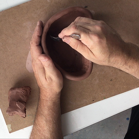 Clay Coils Two hands sculpting a clay pot with a spoon