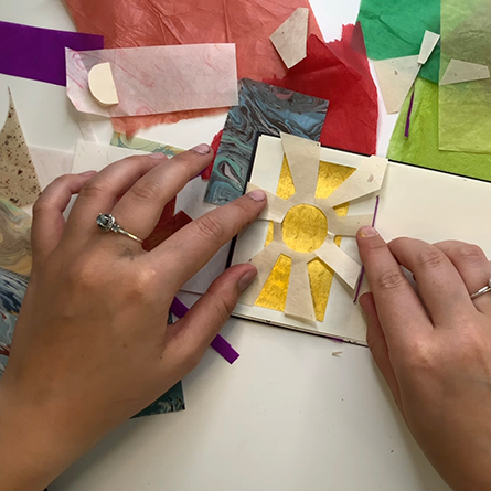 Binding Booklets Two hands gluing a sun shaped cutout into a small binded book